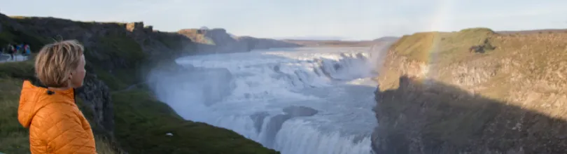 En person i orange jacka ser ut över vattenfallet Gullfoss.