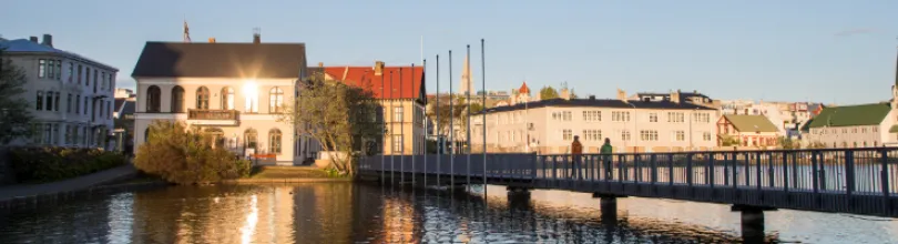 Hus och en gångbro vid Tjörnin i Reykjavík i kvällsljus.