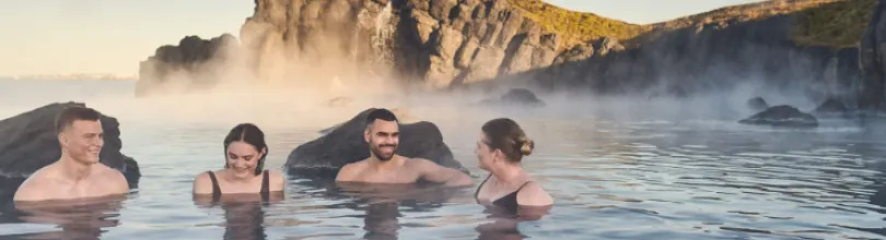 Fyra personer badar i Sky Lagoon bland klippor och vattenånga.