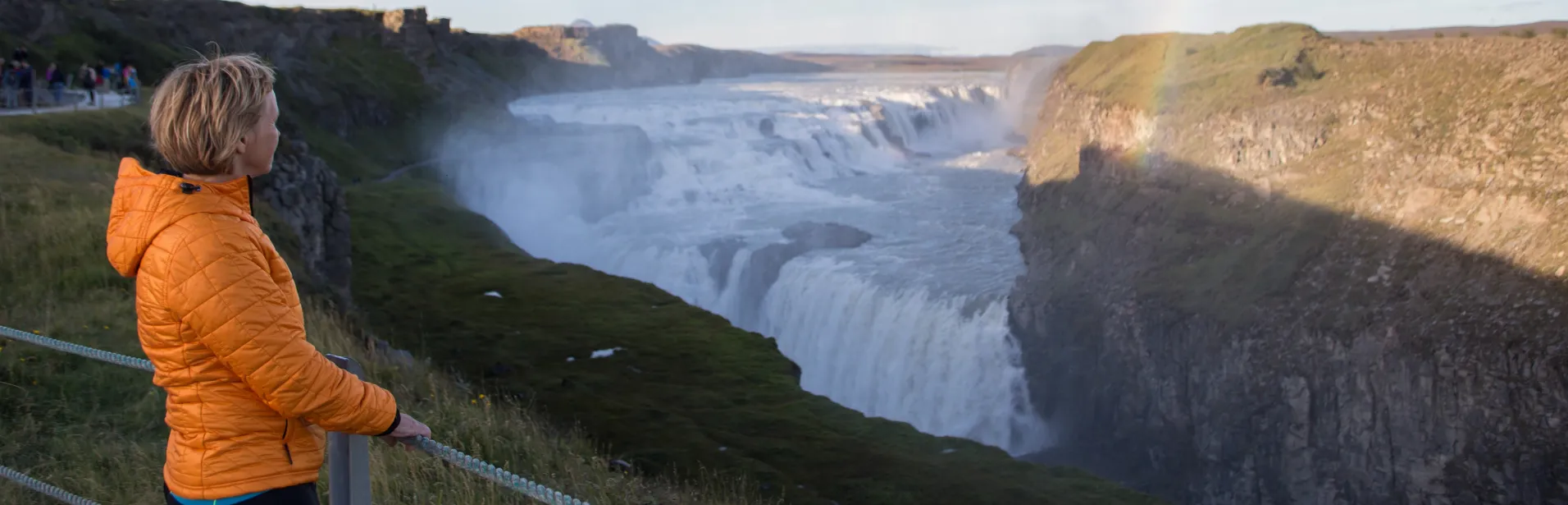 En person i orange jacka ser ut över vattenfallet Gullfoss.