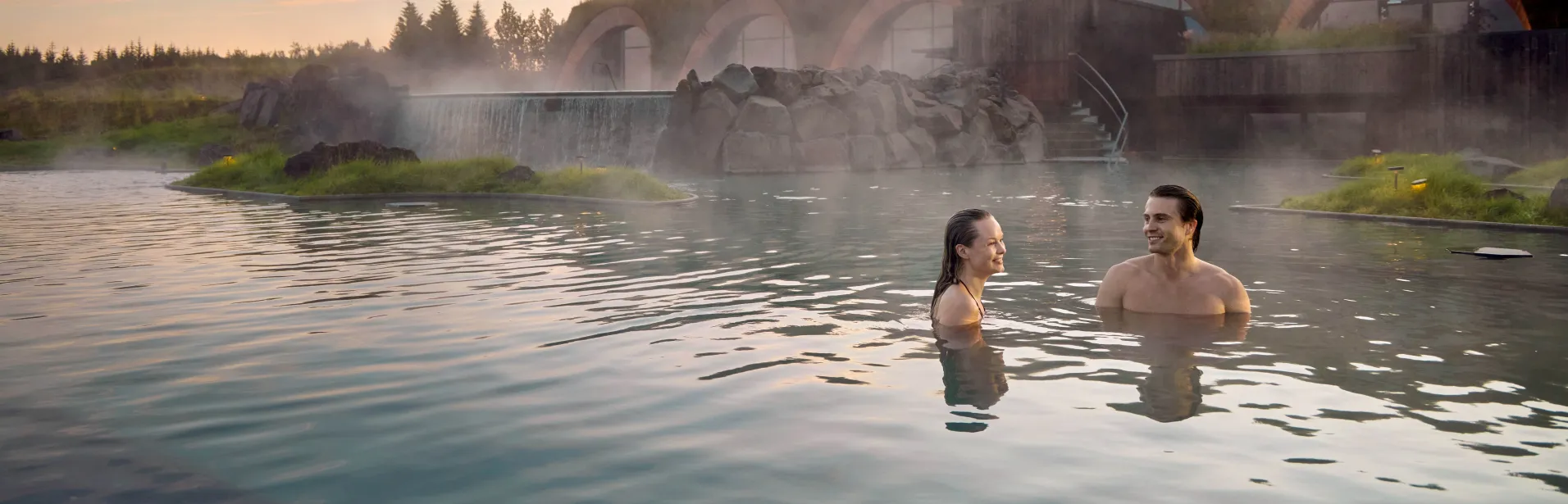 Två personer badar i Laugarás Lagoon med ånga över vattnet.