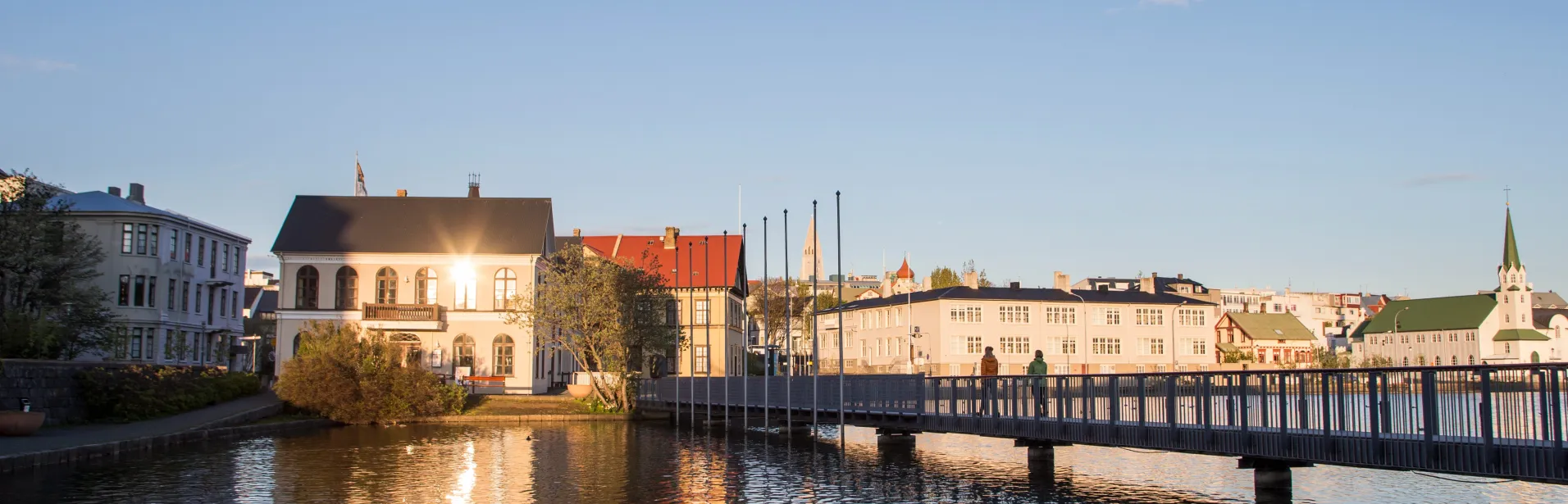 Hus och en gångbro vid Tjörnin i Reykjavík i kvällsljus.