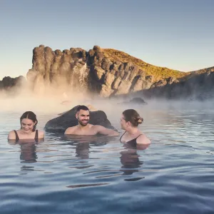 Fyra personer badar i Sky Lagoon bland klippor och vattenånga.
